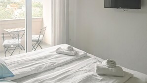 Een hotelkamer met twee bedden, een aan de muur bevestigde televisie, een balkon met een tafel en stoelen, en uitzicht op de omgeving.