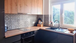 A modern kitchen with wooden cabinets, patterned backsplash, and a window with a view of greenery. - 2 bedroom nice apartment in Rab (Rab)