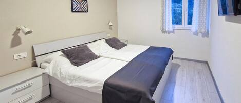 A bedroom with a bed, bedside tables, a wall-mounted air conditioner, a window with curtains, and a wall-mounted TV.