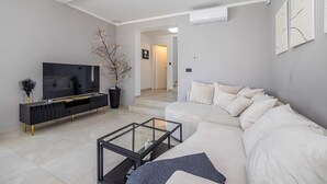A modern living room with a sofa, a glass coffee table, a TV, and a decorative plant. - Villa LA VIE with private pool (Garica)