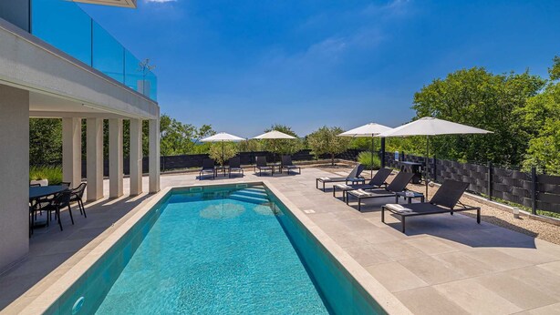 A modern outdoor pool area with lounge chairs and umbrellas, surrounded by a stone wall and greenery. - Villa LA VIE with private pool (Garica)