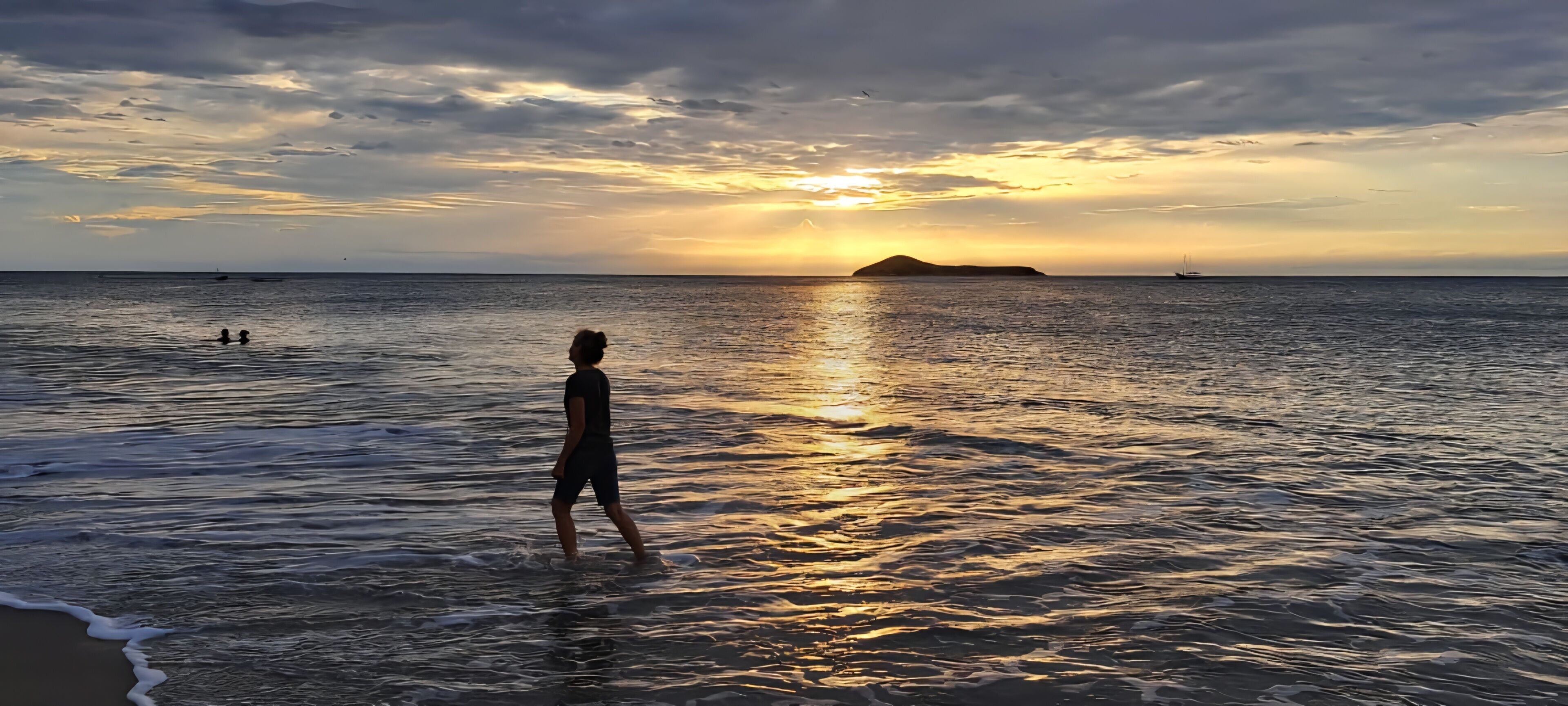 A person standing in shallow water at the beach during sunset.