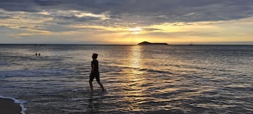 Una persona de pie en aguas poco profundas en la playa durante el atardecer.
