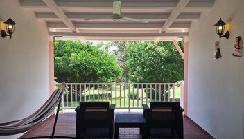 A covered patio with two black wicker chairs, a hammock, and a ceiling fan.
