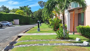 Una calle residencial con césped cuidado, palmeras y una casa moderna.