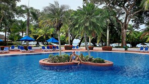 A pool area with blue lounge chairs and umbrellas, surrounded by lush greenery and palm trees. - PLAYA BLANCA GOLF and BEACH VILLA (Rio Hato)