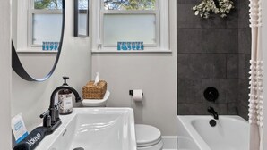 Et badeværelse med en hvid vask, toilet og badekar, et vindue med udsigt til træer, og et spejl.