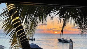 Zonsondergang vanaf een balkon met palmbomen, een tafel en stoelen.