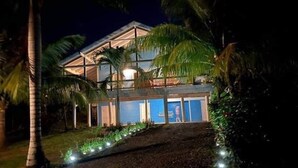 A two-story building with a balcony, surrounded by palm trees and illuminated by string lights. - Beautiful West Bay Beach large 4 br with pool. (West Bay)