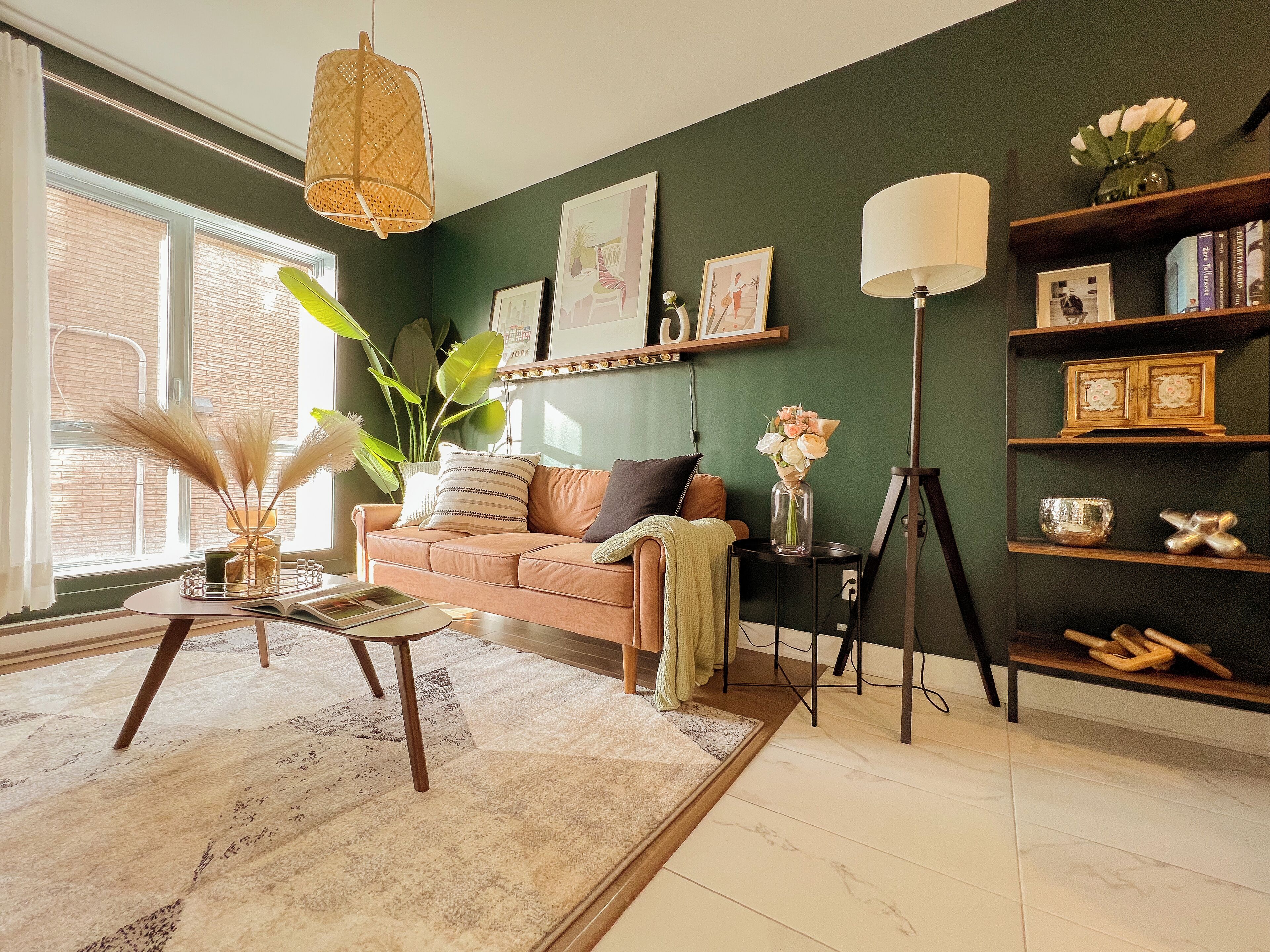 A cozy living room with a green wall, a brown sofa, a coffee table, a floor lamp, and a bookshelf.