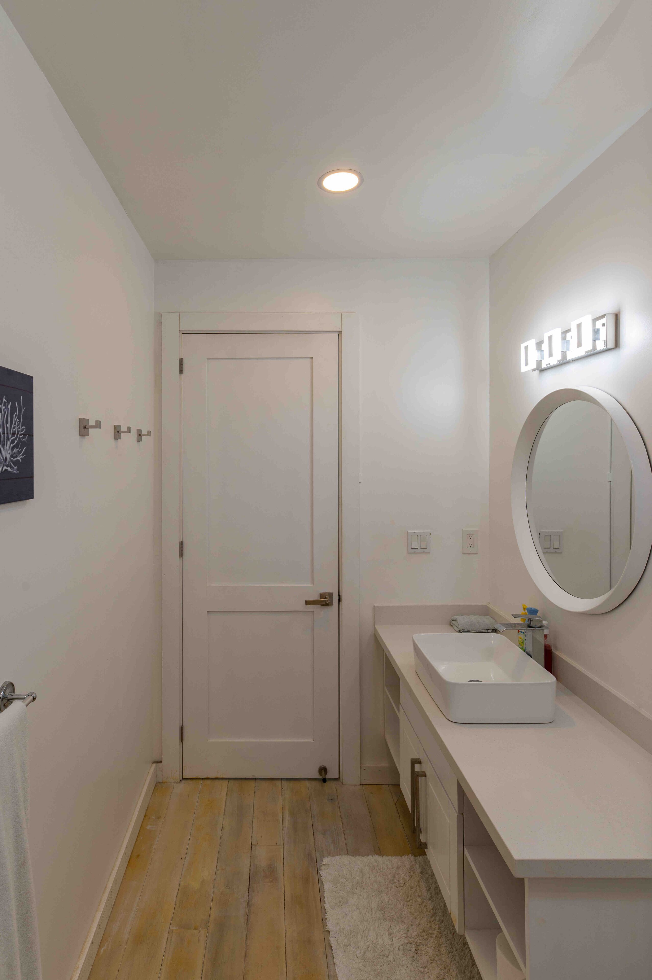 A modern bathroom with a white door, a round mirror, and a white sink.