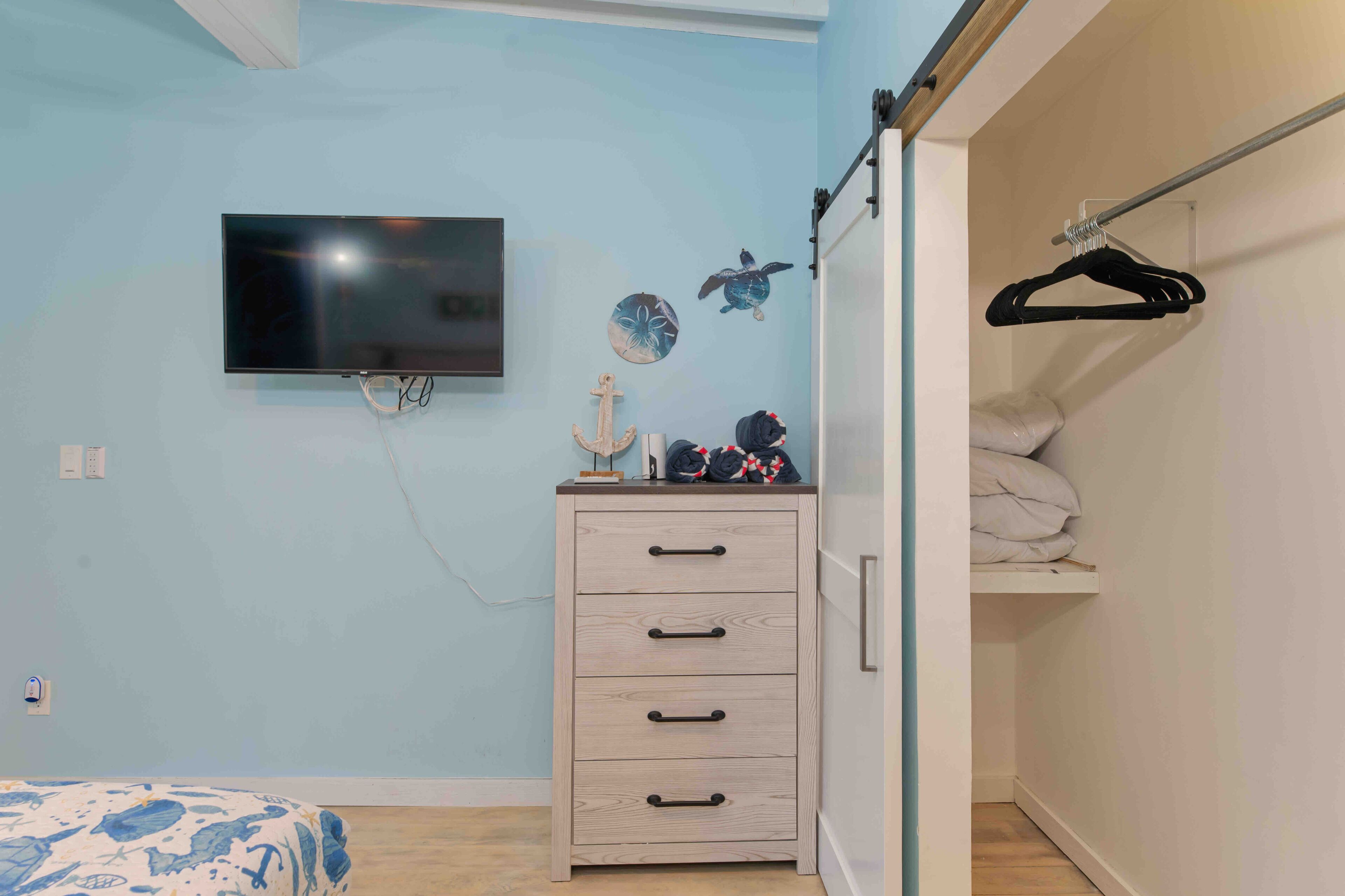 Ein Schlafzimmer mit einem Bett, einem Schminktisch, einem an der Wand befestigten Fernseher und einem Kleiderschrank mit Kleiderstange.