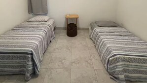 A small, clean room with two single beds, a ceiling fan, and a small wooden stool. - New in market, Hato Rey 2 bedrooms -301- (San Juan)