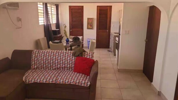 Un salon avec un canapé à motifs, un coussin rouge et un coin repas comprenant une table et des chaises.