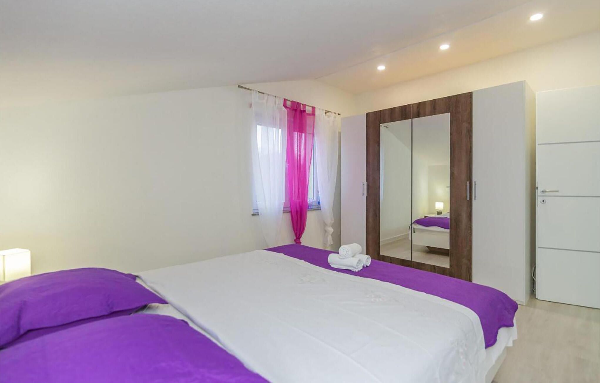 Ein Schlafzimmer mit Bett, Kleiderschrank, Spiegel und einem Fenster mit Vorhängen.