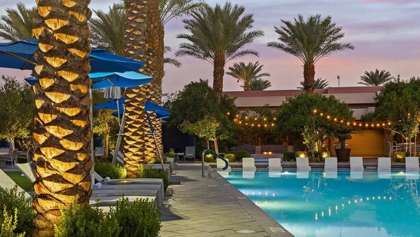 Un espace aménagé au bord de la piscine, avec des chaises longues, des parasols et des palmiers.