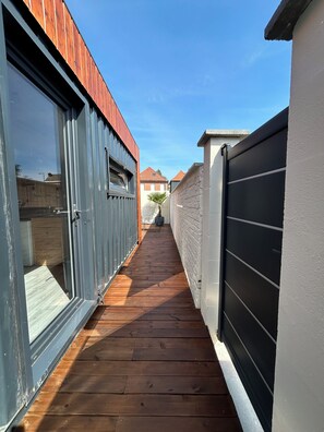 Un étroit sentier en bois mène à un bâtiment moderne doté de grandes portes vitrées et d’un toit en métal.