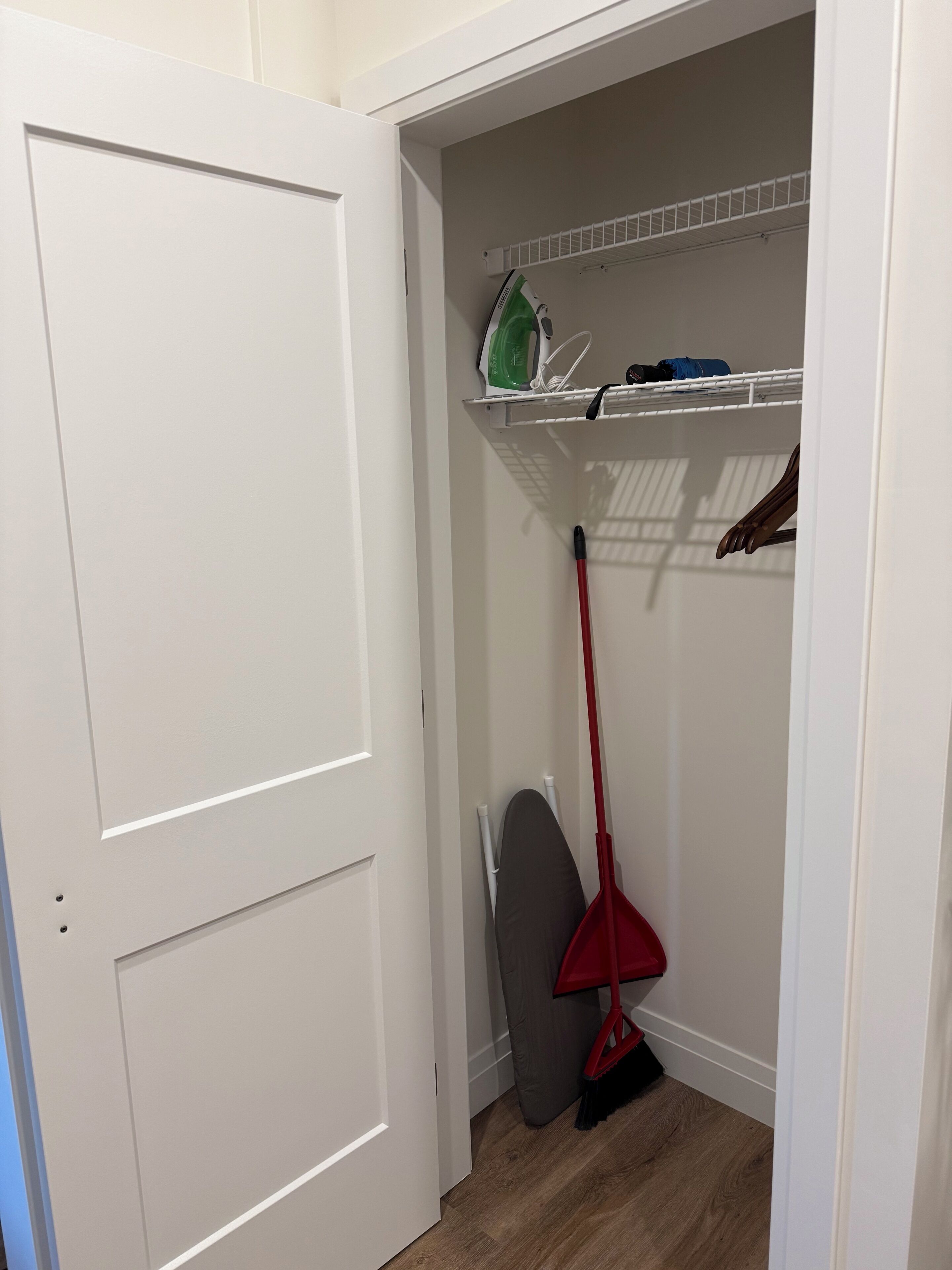 A closet with a hanging rack, a broom, and a shelf with a green iron and other items.