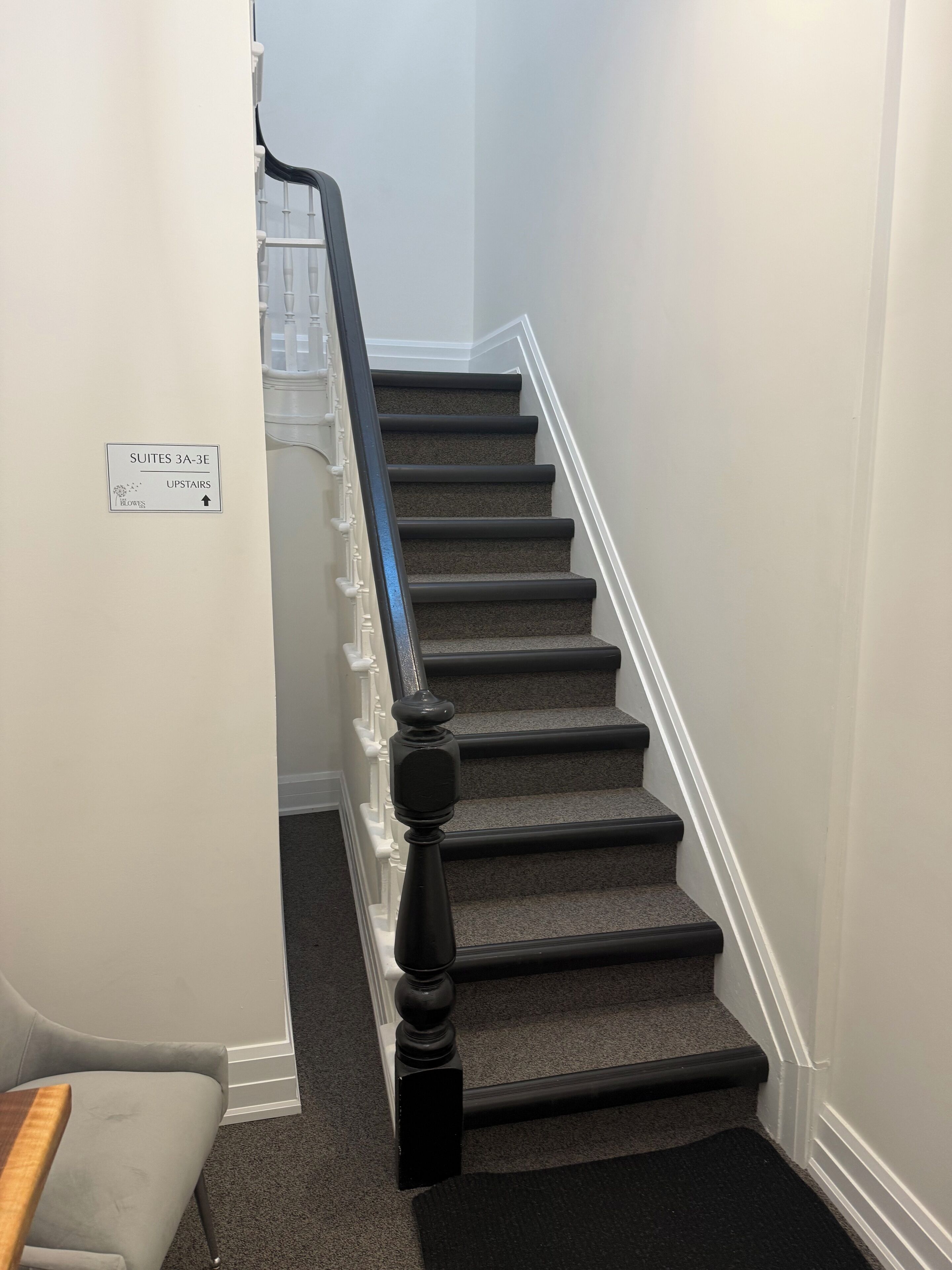 Una escalera con peldaños alfombrados y barandilla, que conduce a un espacio con la indicación 'Suites 3A-3E Arriba'.
