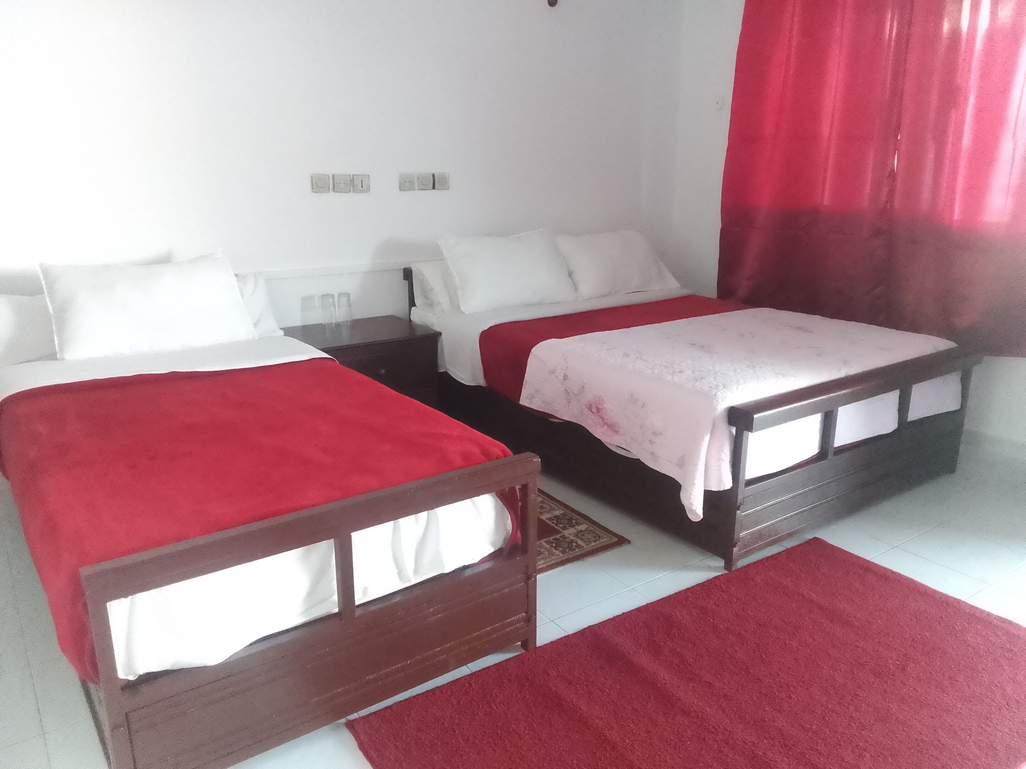 Une chambre d’hôtel avec deux lits, une moquette rouge et un mur blanc équipé de prises électriques.