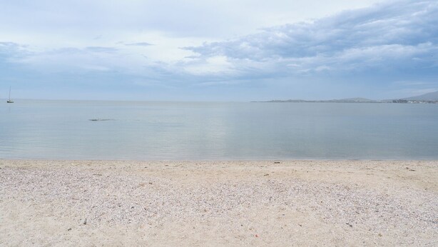 Une plage aux eaux calmes, un voilier et une terre lointaine à l’horizon.
