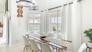 Un espace repas avec une longue table en bois, des chaises blanches et un lustre.