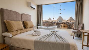 A hotel room with a large bed, a bathtub, a view of pyramids, and a cityscape.