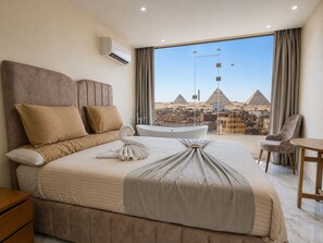 Een hotelkamer met een groot bed, een badkuip, uitzicht op piramides en een stadsbeeld.