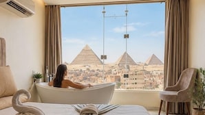 A hotel room with a bed, a bathtub, and a view of the pyramids. - Amon Ra Hotel (Giza)