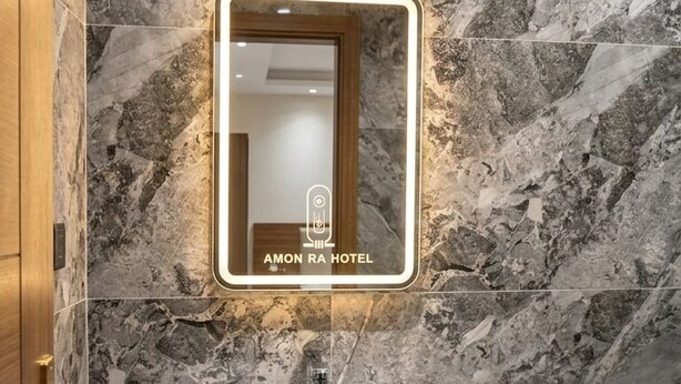 A bathroom with a marble wall, a mirror, and a sink with a black cabinet. - Amon Ra Hotel (Giza)