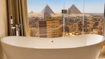 A bathroom with a freestanding bathtub, a window with curtains, and a view of the pyramids.