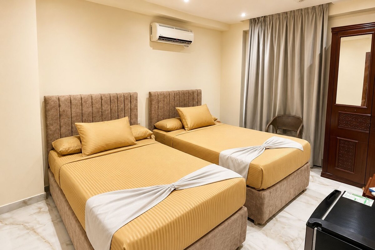 A hotel room with two beds, a wooden door, an air conditioning unit, and a chair.