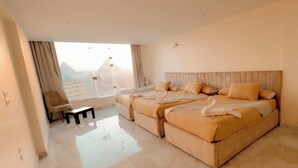 A bedroom with a large bed, a small table, and a view of the city. - Amon Ra Hotel (Giza)