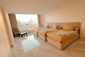 A bedroom with a large bed, a small table, and a view of the city. - Amon Ra Hotel (Giza)