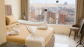 Une chambre d’hôtel équipée d’un lit, d’un bureau, d’une chaise, d’un réfrigérateur et offrant une vue sur un paysage urbain avec une pyramide.