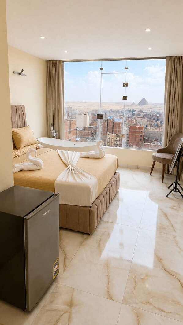 Une chambre d’hôtel équipée d’un lit, d’un bureau, d’une chaise, d’un réfrigérateur et offrant une vue sur un paysage urbain avec une pyramide.