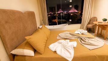 A hotel room with a bed, a chair, a small table, and a view of the pyramids at night.