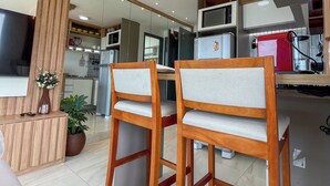 Een moderne keuken met houten kasten, een magnetron en een koelkast. Er staan twee houten stoelen met beklede zitplaatsen.
