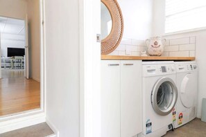 Un lavadero con lavadora, secadora, repisa de madera con un objeto decorativo y un espejo en la pared.