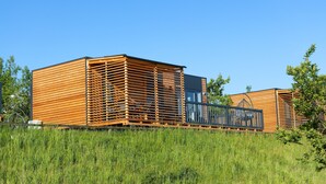A modern wooden cabin with a slatted exterior, a balcony, and a clear blue sky in the background. - Modernes Mobilehome im Vital Camp Bayerbach (Bayerbach)
