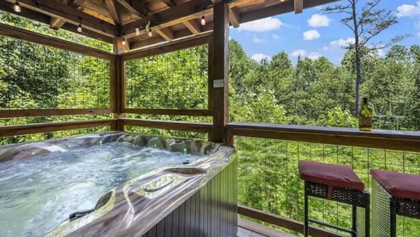 A hot tub on a wooden deck with a view of a forest. - Black Bear Bungalow by Beyond Expectations (Gatlinburg)