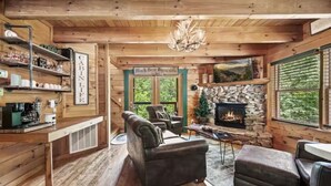 A cabin interior with a fireplace, wooden furniture, and a view of the outdoors. - Black Bear Bungalow by Beyond Expectations (Gatlinburg)