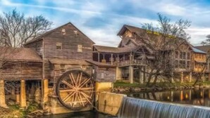 A historic water mill with wooden buildings, a large water wheel, and a small waterfall. - Black Bear Bungalow by Beyond Expectations (Gatlinburg)