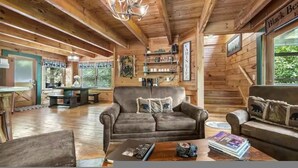 A cozy cabin interior with wooden walls, a fireplace, a sofa, and a dining area. - Black Bear Bungalow by Beyond Expectations (Gatlinburg)