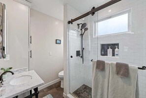 A modern bathroom with a glass-enclosed shower, a white sink, and a small window above the mirror. - Coastal Retreat in the Heart of Capitola Village - Steps from the Beach! (Capitola)