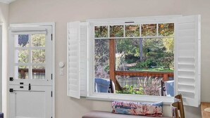A room with a white door, a window with shutters, a bench, and a view of a garden. - Coastal Retreat in the Heart of Capitola Village - Steps from the Beach! (Capitola)