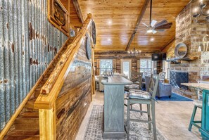 A rustic interior with a wooden staircase, a dining area, and a kitchen with stone walls. - Frio Hills Hideaway | Creek | Mountain Views (Leakey)