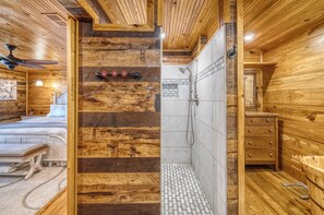 A wooden interior with a shower area, wooden cabinets, and a bed with a headboard. - Frio Hills Hideaway | Creek | Mountain Views (Leakey)