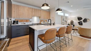 Una cucina moderna con mobili in legno, un'isola centrale con sgabelli da bar, illuminazione a sospensione e un'area pranzo con divano.