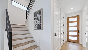 Una scala con gradini in legno e ringhiere nere, un muro bianco con un quadro incorniciato e una porta in legno con pannelli di vetro.
